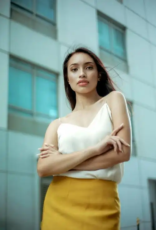 女人的选择聚焦照片在白色的顶部和黄色的裙子摆在建筑物外,她的双手