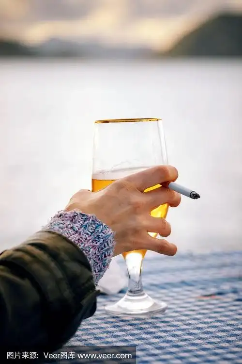 一个女人的手拿着一杯啤酒和一根香烟与模糊的大海,天空和岛屿背景在