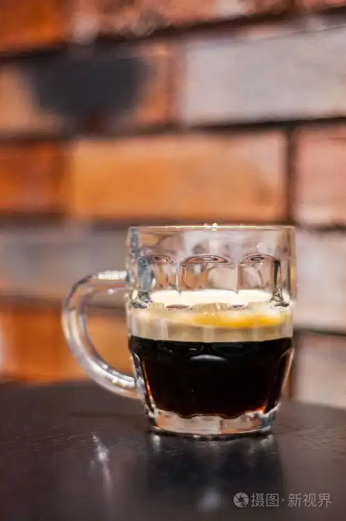 在砖墙背景上的酒吧里的木桌上,用一杯深色啤酒照片-正版商用图片13y