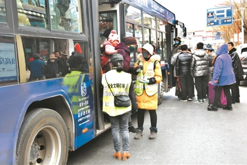 图为在娘热路民航局公交站,两位安全文明引导员正在扶一位背着孩子