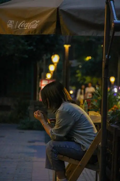 夜晚室外灯火阑珊,一个年轻短发女孩安静的坐在凳子上玩手指,安详