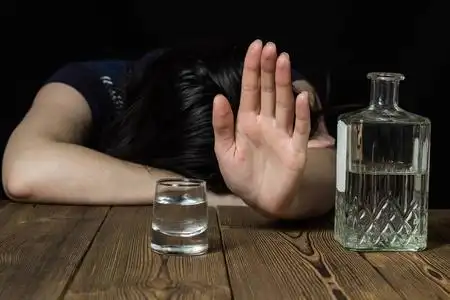 醉酒的女孩躺在桌子上, 手上显示停止, 黑色背景, 桌上的酒精照片