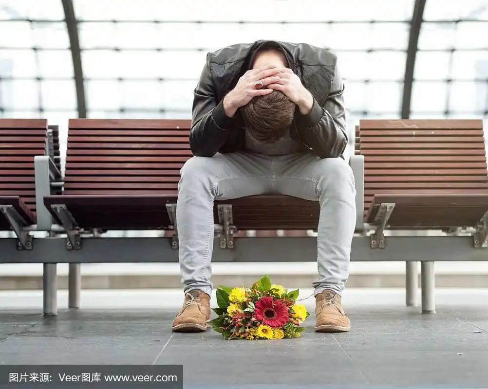 一个悲伤的男人独自低着头坐在火车站里