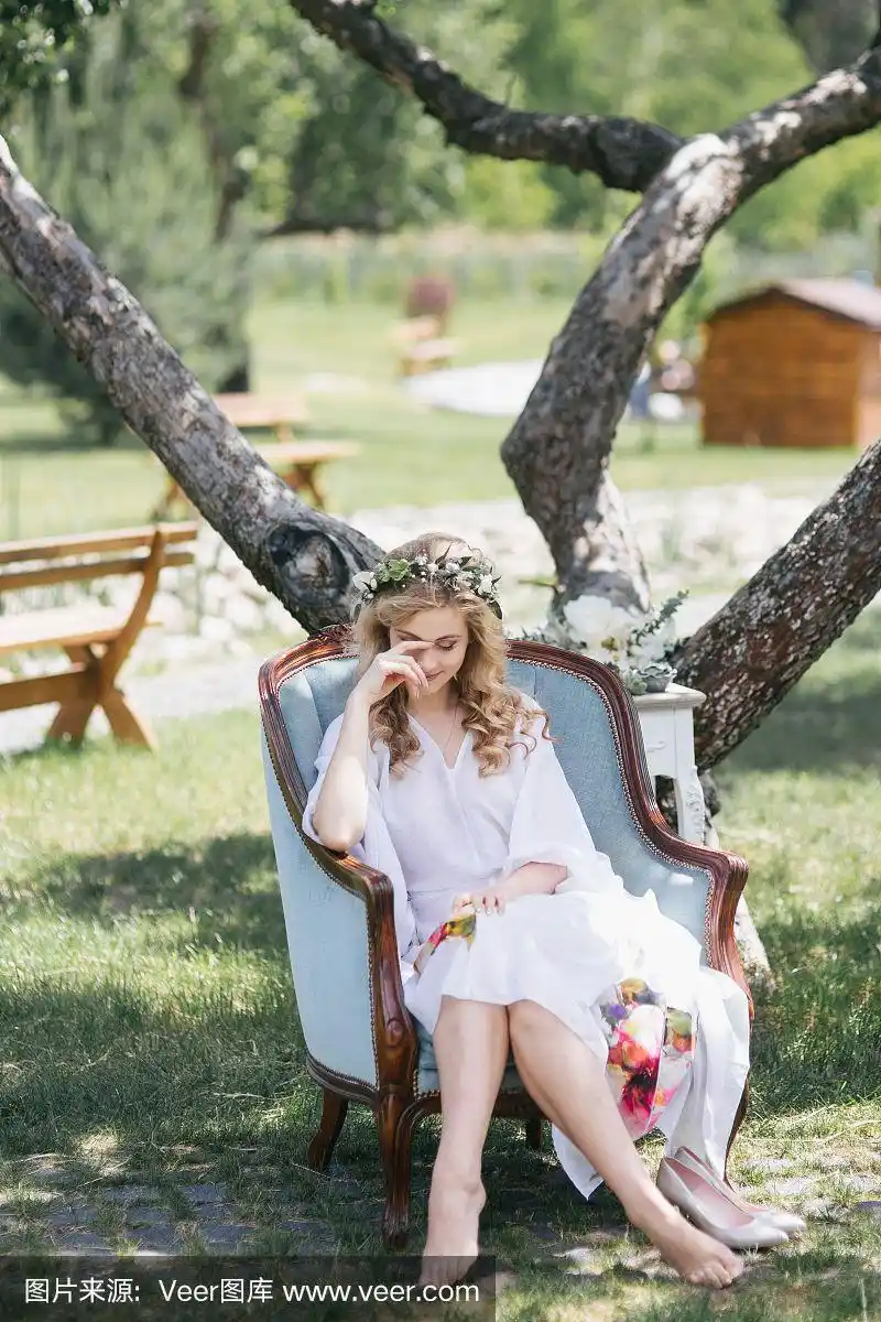 美丽的年轻赤脚新娘在花圈坐在扶手椅上婚礼前