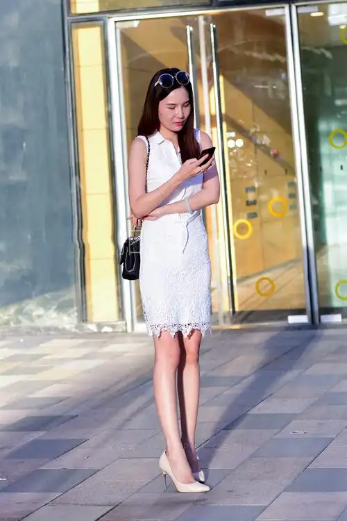 这位看手机的小姐姐,身材高挑,身穿白色连衣裙搭配尖头高跟鞋,释放