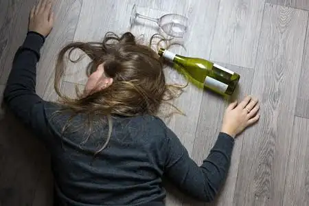 言难而上宿醉酒的年轻女孩躺在地板上因为喝红酒空玻璃和瓶子而感到