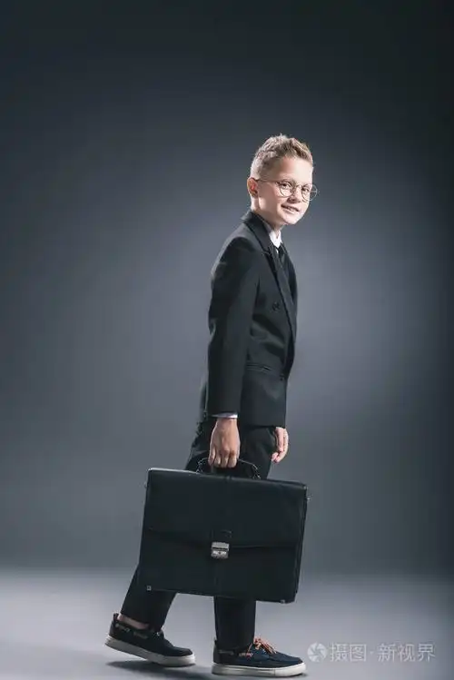 青春期前男孩的侧面视图在生意人西装和眼镜与手提箱在黑暗背景