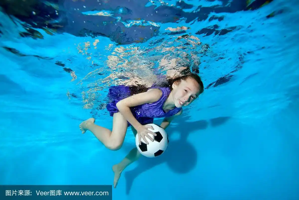 快乐的小女孩游泳和玩水下足球.