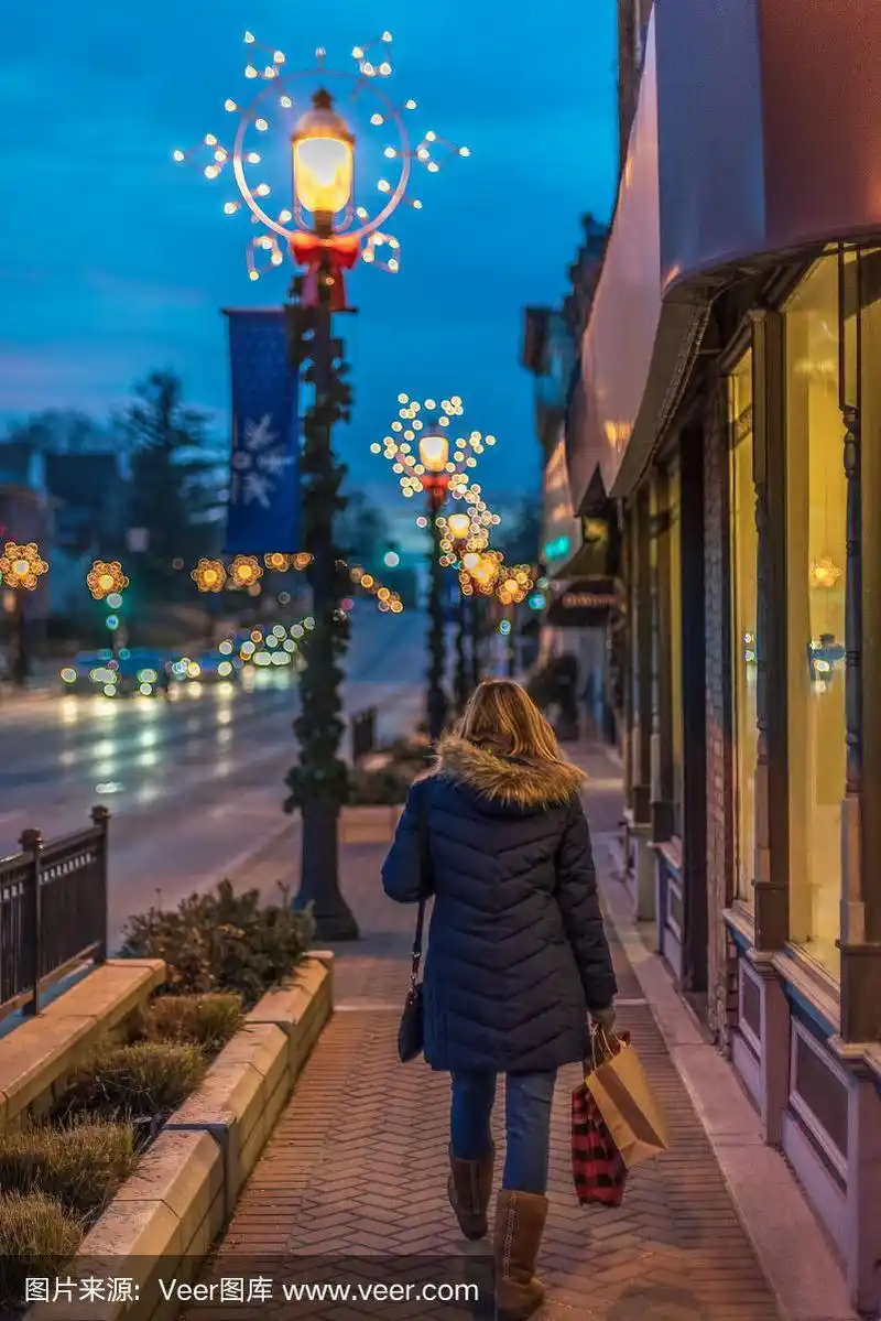 在圣诞节期间挎着购物袋的女人在市中心行走的背影