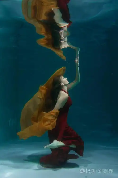 一个美丽的自由潜水员,一个人穿着红色的长裙,独自在深水中