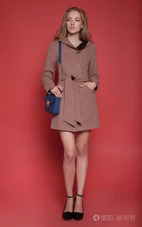 美丽的年轻女子,穿着外套红色背景上摆姿势