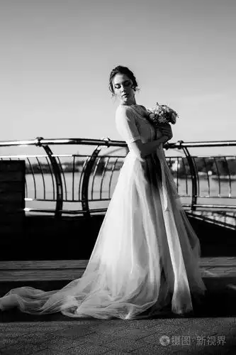 戏剧性的黑色和白色的新娘婚纱礼服和花束站在河岸上的肖像