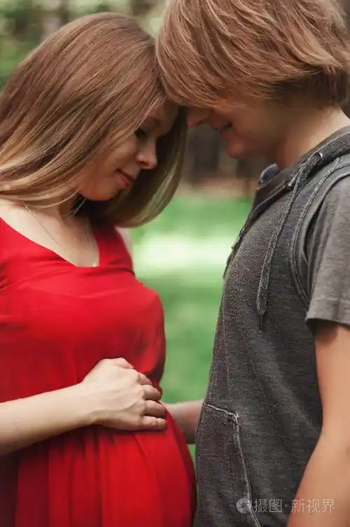 垂直照片.一对幸福的夫妻丈夫拥抱一个漂亮的成年怀孕妻子.