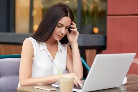 横拍相当忙碌的女性自由职业者坐在打开的笔记本电脑前,喝咖啡,在新