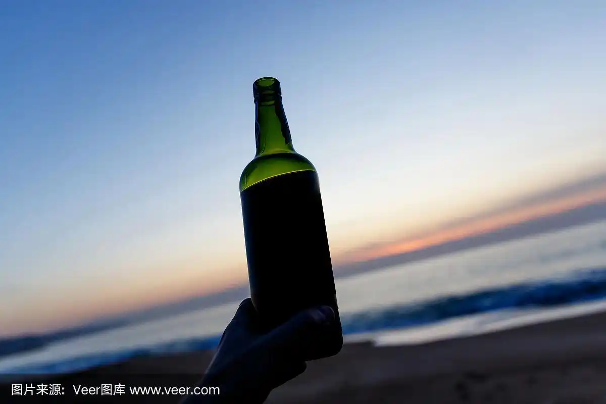 夕阳下,一个男人的手拿着酒瓶