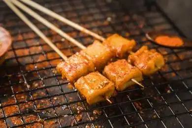 黑色烤架上放着几串撒着辣椒面油炸鱼豆腐