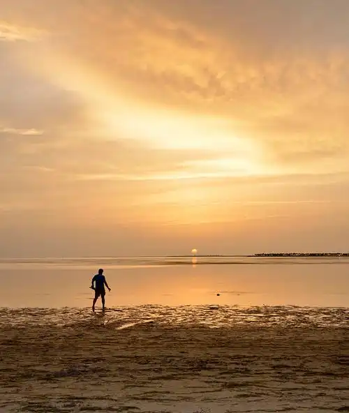 在橙色天空下的海滩上行走的剪影男人图片
