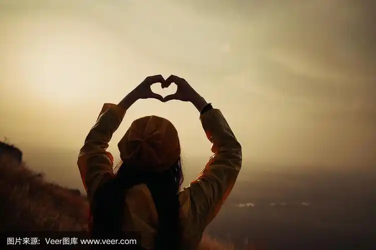 一个年轻的女孩在日落时用她的双手做心形的象征
