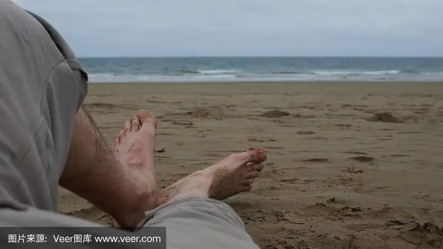 一个男人光着脚躺在沙滩上,背景是大海