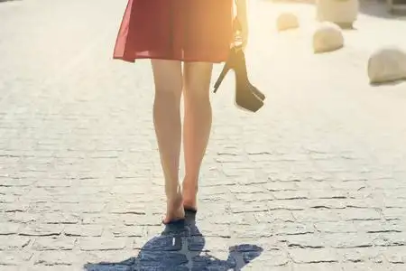 穿红衣服的女士, 手里拿着高跟鞋, 赤脚走在街上.