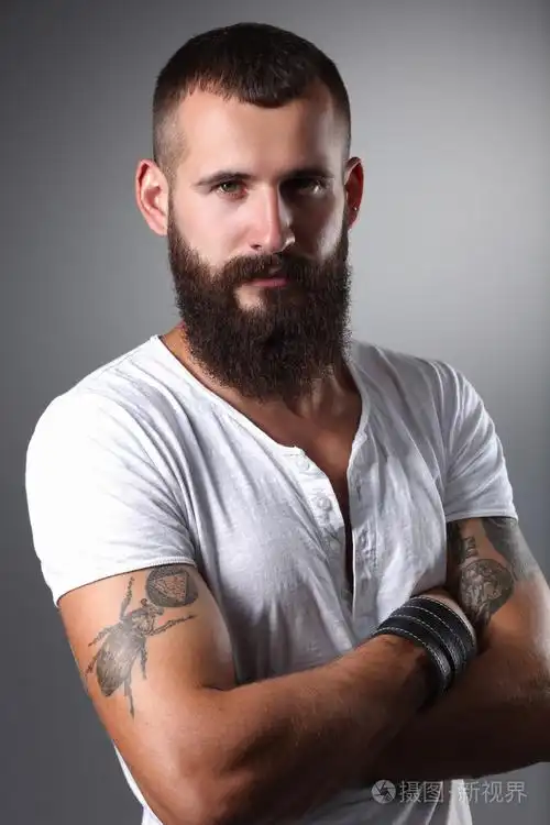 英俊的大胡子男人站着双臂交叉,灰色的背景上孤立的肖像