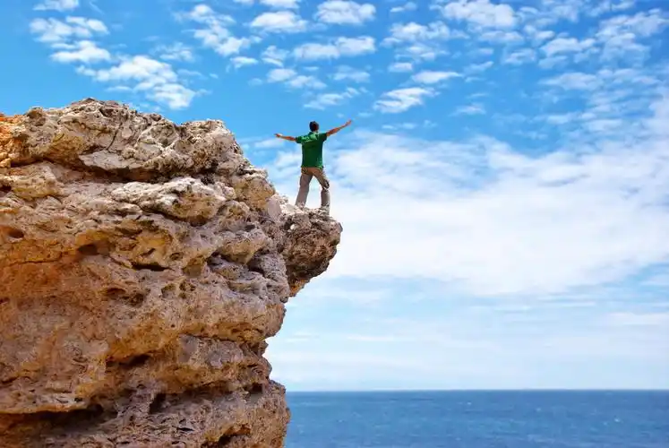 蓝天大海背景男子张开双臂在悬崖的边缘上