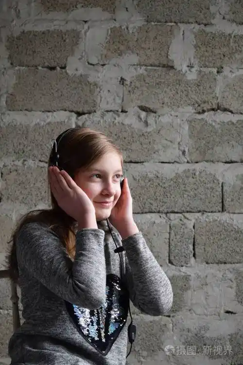 一个愉快友好快乐的少年戴着耳机听音乐的概念肖像年轻的女孩穿着一件