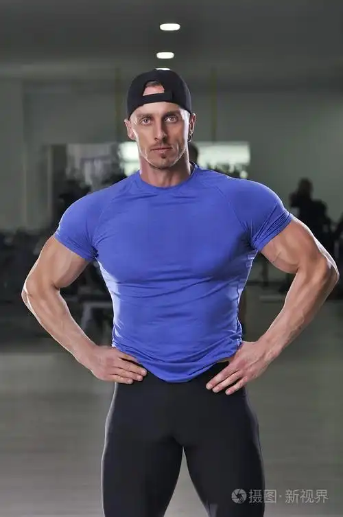 帅强大健壮的男人在健身房里摆姿势.与完美手臂和胸部肌肉强壮健美