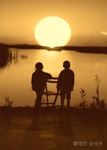 男孩和女孩在日落时在河上.剪影