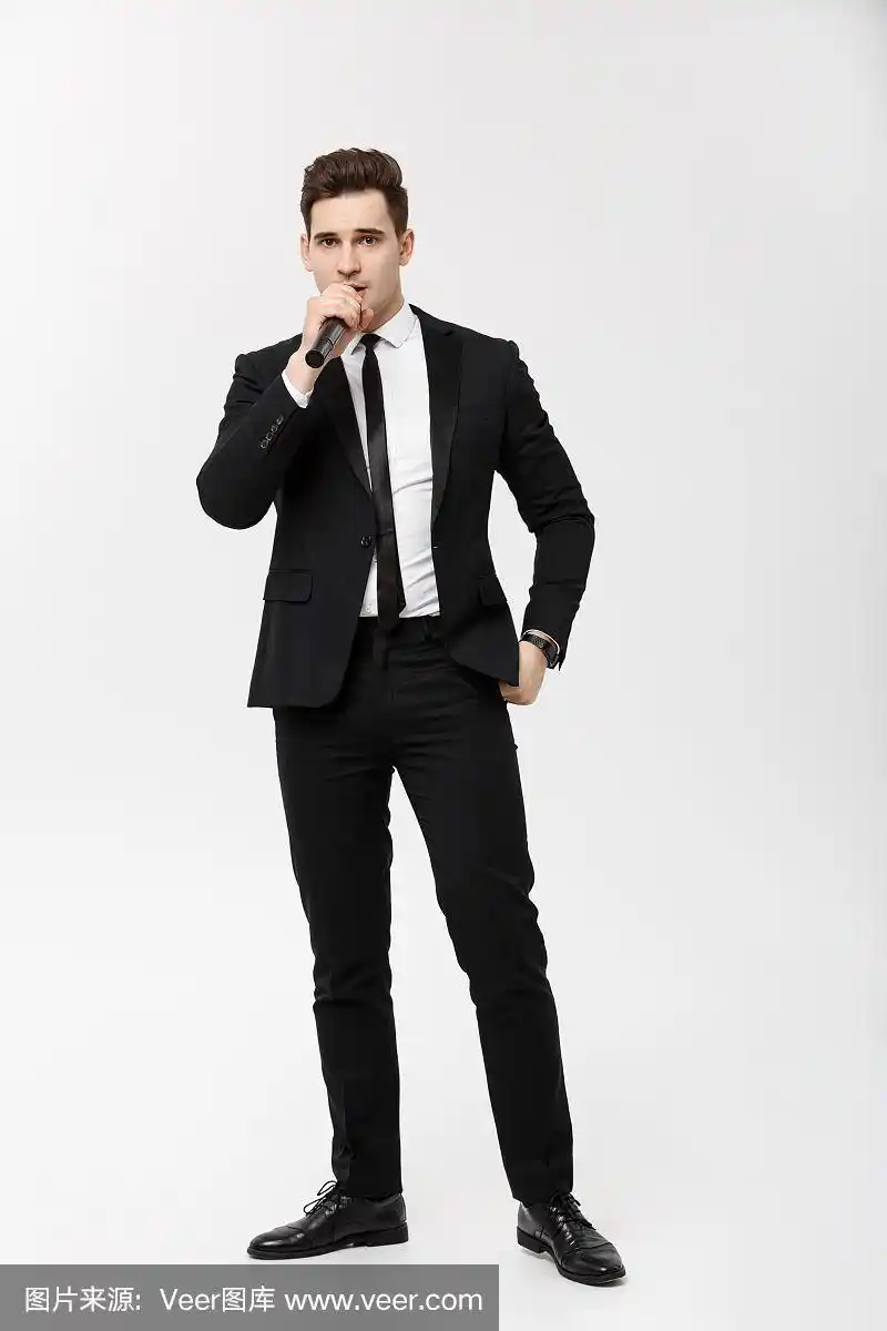 经营理念:全身肖像年轻男子在黑色西装拿着麦克风,唱歌和摆姿势对着