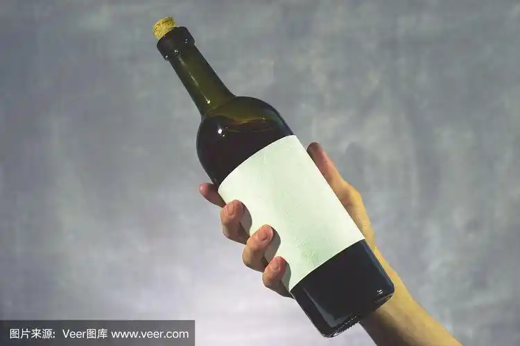 手持红色酒瓶与白色纹理标签在一个美丽的背景.