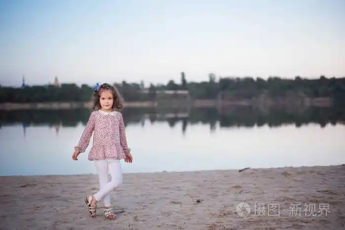 在湖边白色长裤的时髦女孩孩子在沙子上赤脚花钱美丽的小女孩在水库
