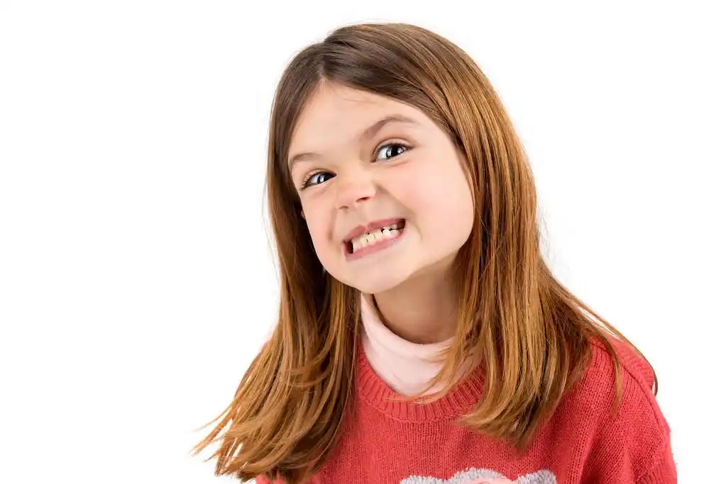 有趣的面孔,可爱的小女孩穿着白色的衣服独自做着鬼脸