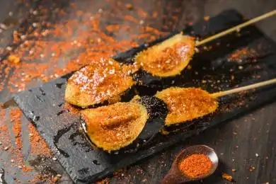 黑色烤架上放着两串撒着辣椒面油炸茄子片