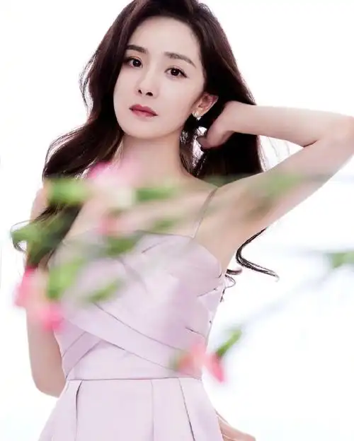 照片中,杨幂身穿粉色绸缎连衣裙,搭配大波浪卷发,手拿鲜花,气质温柔.