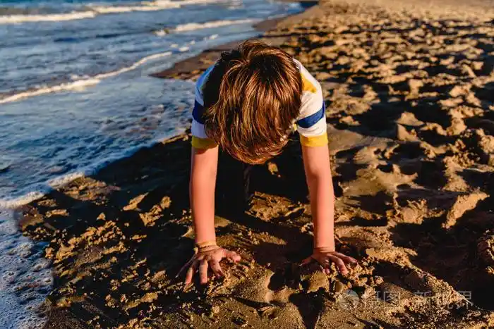 孩子在沙滩上的沙滩上玩耍跪着掩面