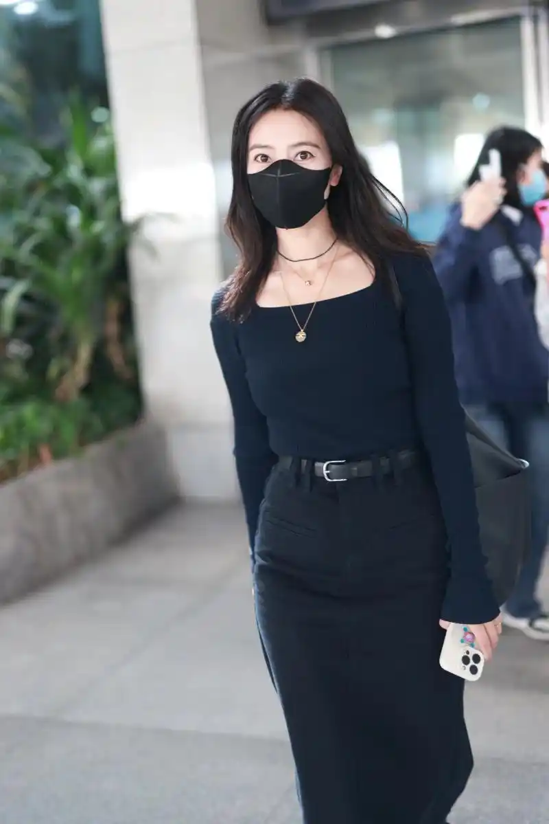 高圆圆机场街拍,身穿紧身的黑色针织衫,搭配黑色半身裙,脸上洋溢着