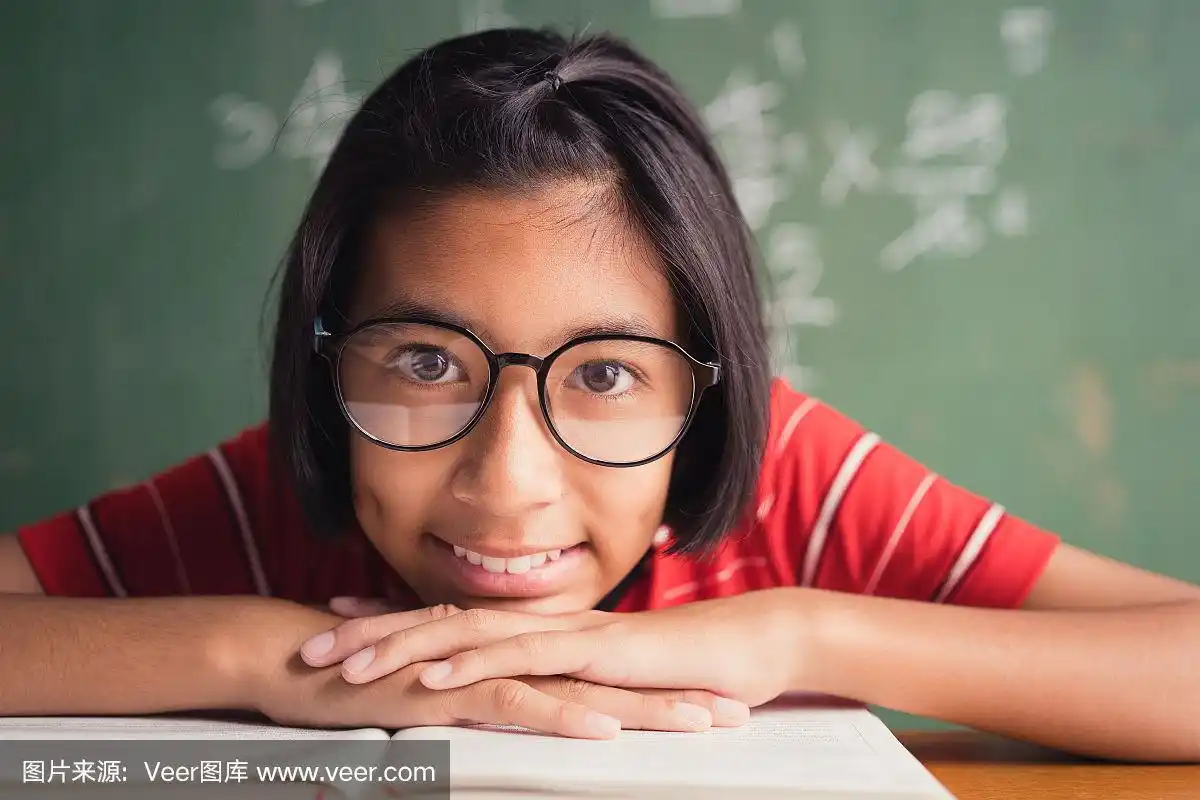 一个戴眼镜的亚洲女孩正在课堂上的黑板上微笑着看书