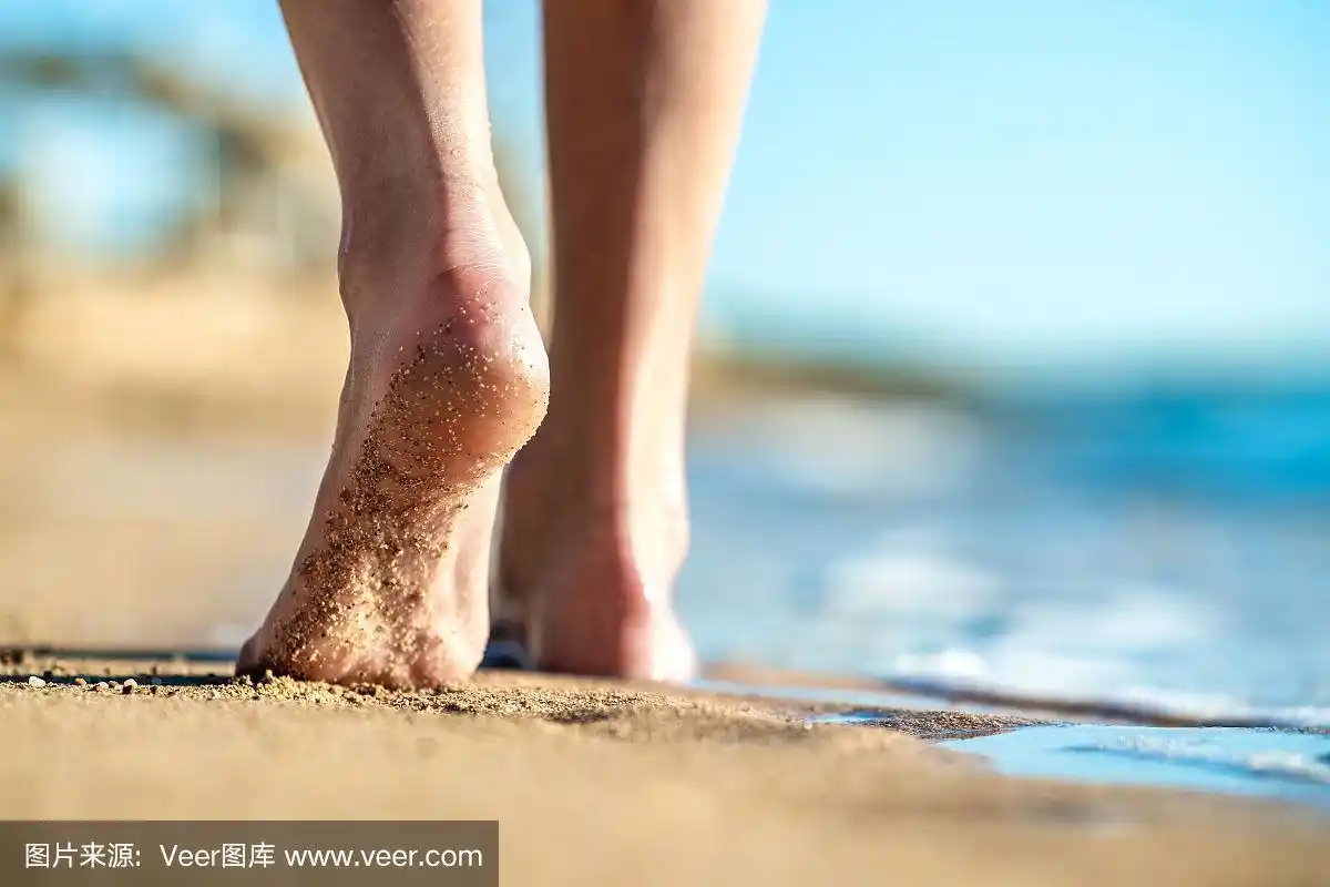 近距离的女人的脚赤脚走在沙滩上留下脚印在金色的海滩.