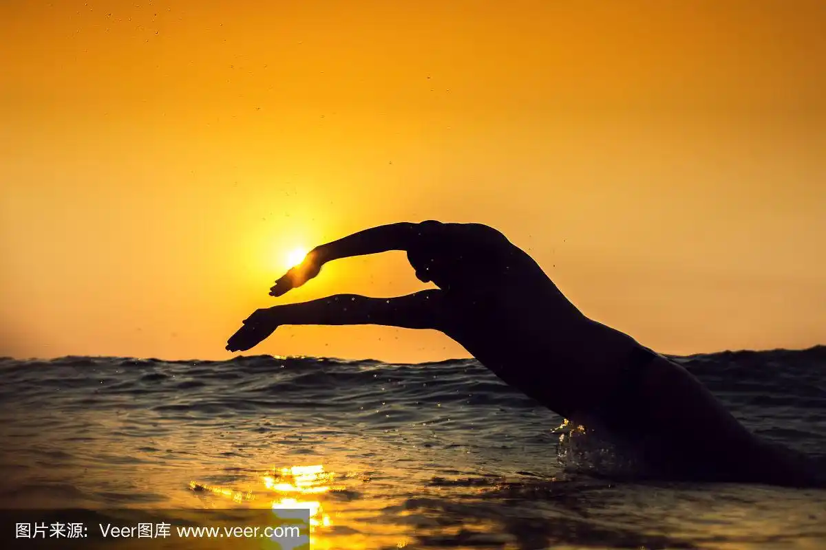 年轻人在大海里游泳,越过黄澄澄的日出