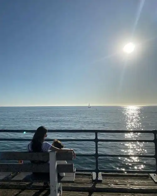 在一片海面上,太阳悬挂在天空中,阳光洒在海面上泛着金光,在海边一个