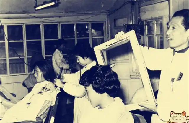 理发师正在为一个妇女烫发,其他街坊邻居都前来观看,效果好估计也