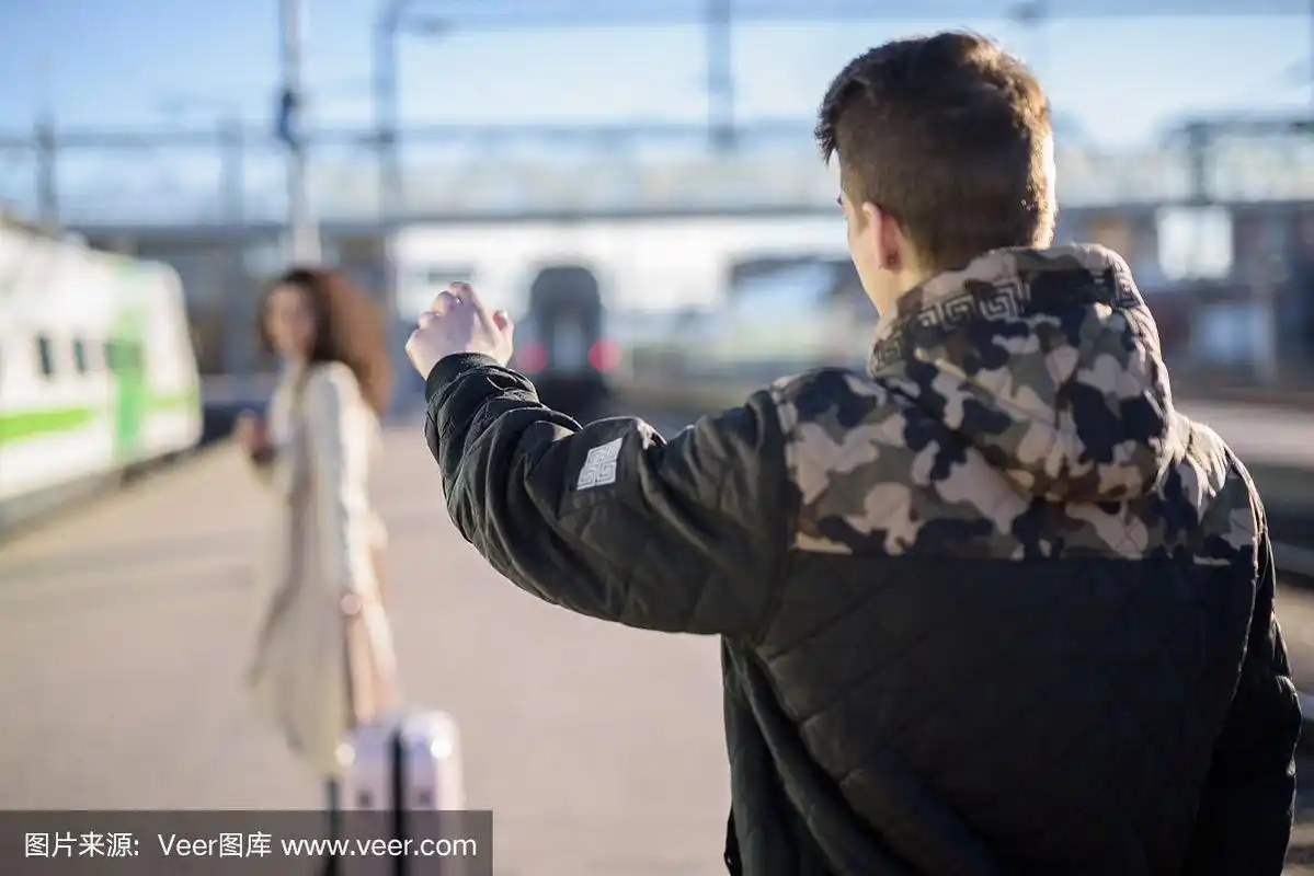 年轻的一对女子带着行李箱在火车站站台离开,男友挥手告别
