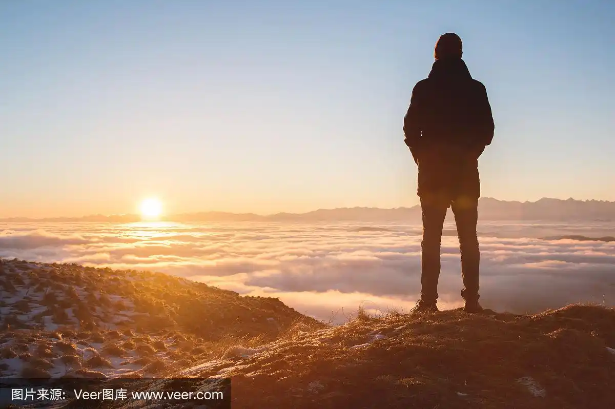 一个孤独的站在山上的人看着夕阳和日落的地平线和充满云的山谷.