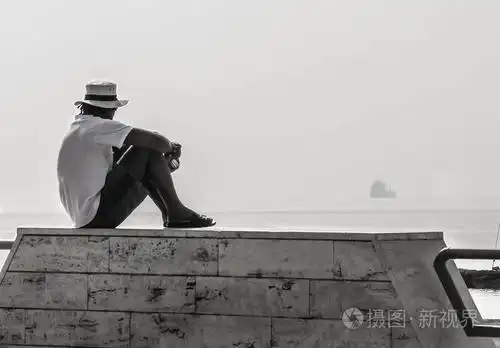 一个人坐在那不勒斯长廊看着远处的大海和一艘小船的灰度照片