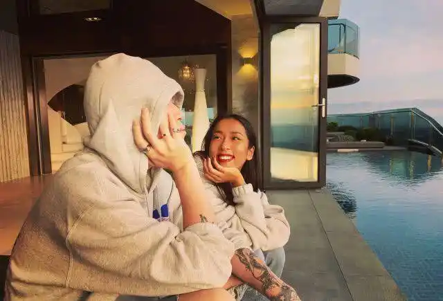 男助理戴着帽子坐在泳池边,吉克隽逸用手撑着脸蛋看着男助理,吉克隽逸