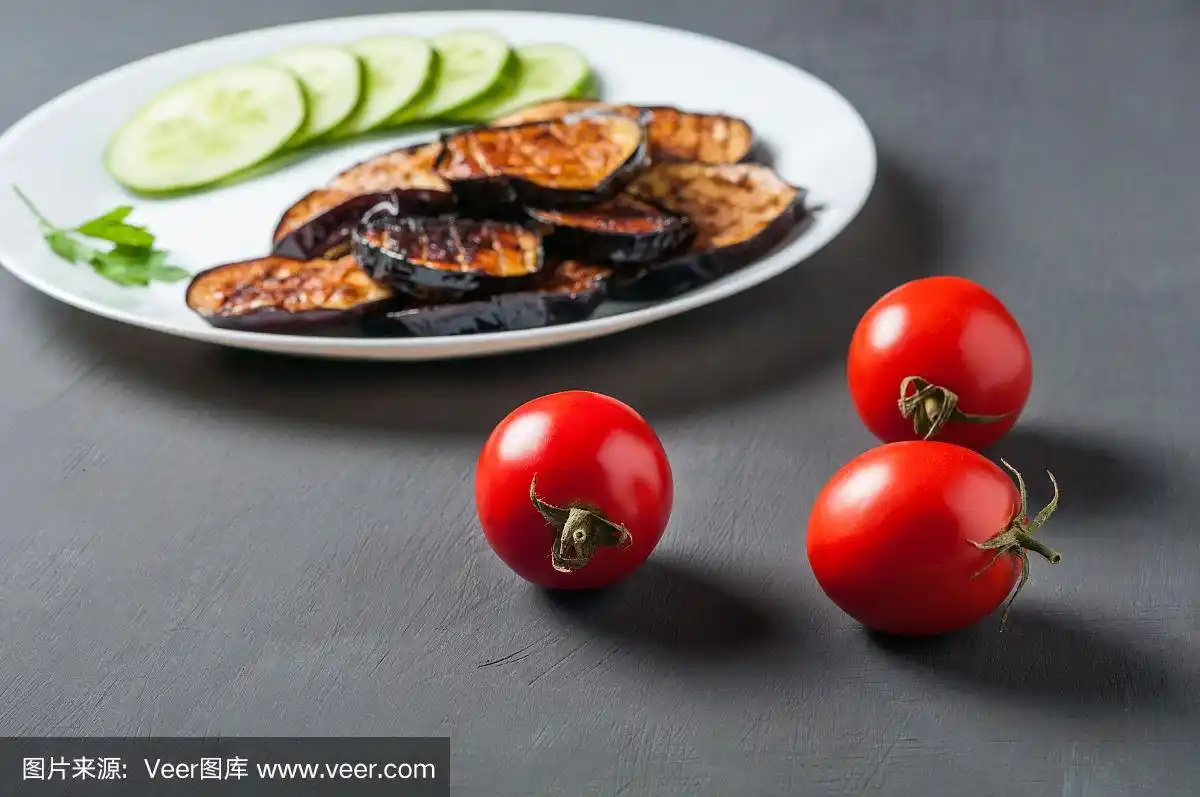 三个完整的新鲜番茄和烤茄子的盘子背景躺在划痕的深色混凝土上