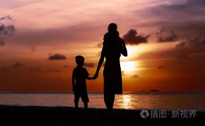 母亲和两个孩子在日落时在海滩上行走