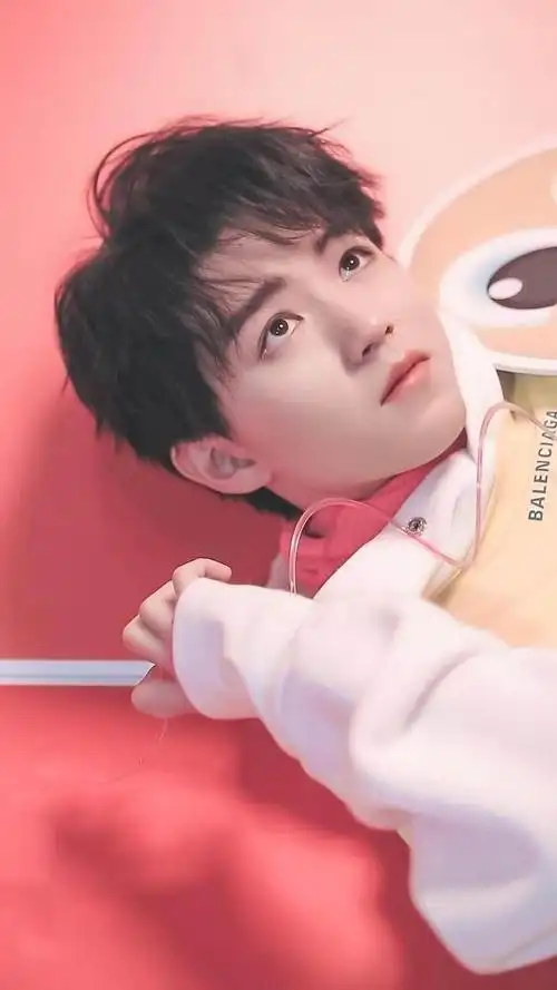 王俊凯躺在红色背景的地方,手自然地放到耳边,表情无辜又呆萌