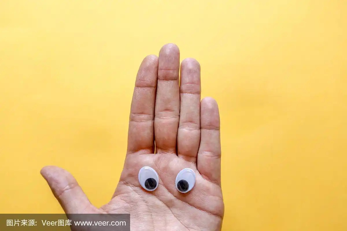 人的手掌上用塑料眼睛做成的笑脸,背景是橙黄色.